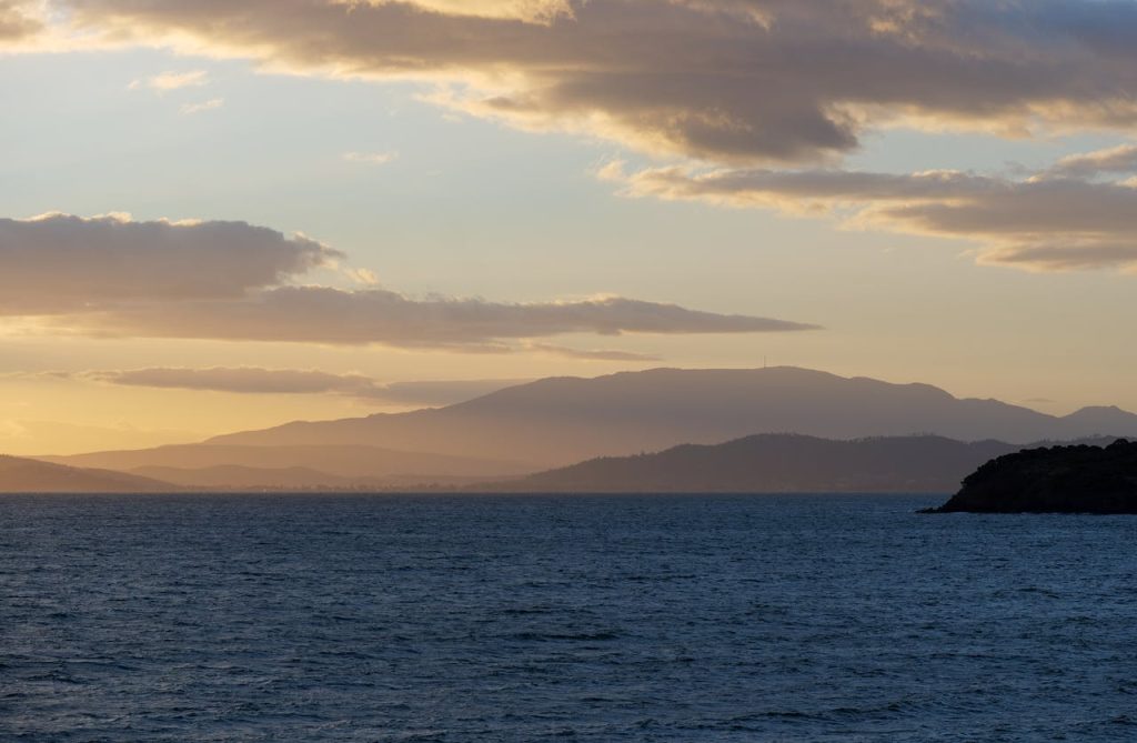 Beautiful sunset over the Tasmanian coastline with Hobart skyline in the distance, showcasing vibrant skies and calm waters.